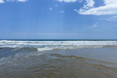 Parlak mavi gökyüzü ve kabarık bulutları ile güzel sahil rahatlamaya ve eğlenceye davetiye çıkarıyor