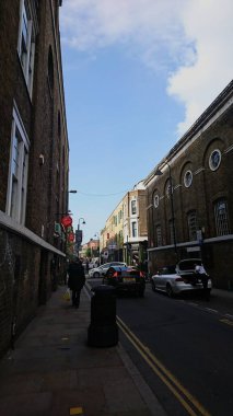 Londra, İngiltere - 14 Mayıs 2018: Brick Lane Pazarı 'nda yayaların yürüdüğü ve güneşli bir yaz gününden önce arabaların güneş ışığı altında geçtiği bir cadde