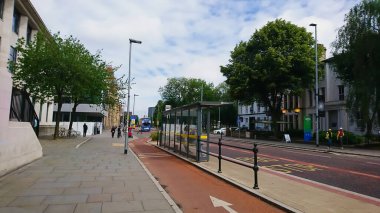 Manchester, Birleşik Krallık - 18 Haziran 2018: Manchester Üniversitesi kampüsünde bulutlu bir gökyüzünün altında otobüs bekleyen yolcularla birlikte bisiklet yolunun yanındaki otobüs durağında.