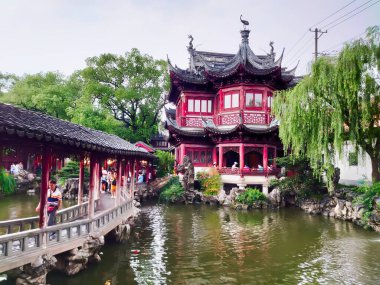 Yu Garden, Şangay, Çin - 24 Haziran 2019: Salgından önce bulutlu bir gökyüzünün altında seramik çatı ve fenerlerle süslenmiş, huzurlu bir göl üzerinde bulunan yürüyüş köprüsü