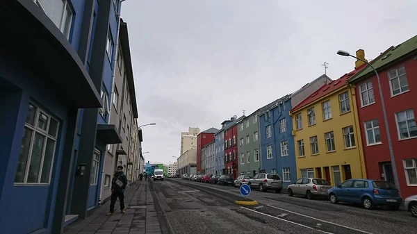 Reykjavik, İzlanda - 27 Mart 2018: Salgından önce şehir merkezindeki bir sokakta renkli evler bloğu ve kaldırımda bulutlu bir gökyüzünün altında yürüyen bir yaya