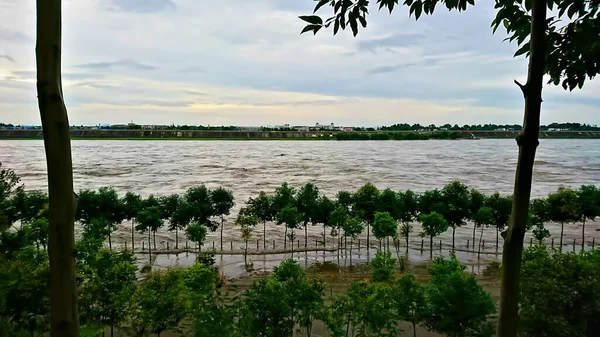中国四川省梅山市鵬山区江コウ町2018年7月11日 木々の列を持つ川の銀行から曇りの空の下で大雨の後に圧倒的な水を持つ川が浸水 — ストック写真