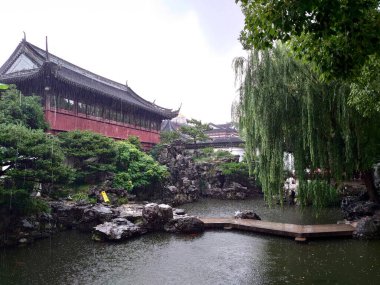 Yu Garden, Şangay, Çin - 24 Temmuz 2019: Çin mimarisi ve söğüdü ile çevrili bir kaya göleti üzerindeki bir köprü