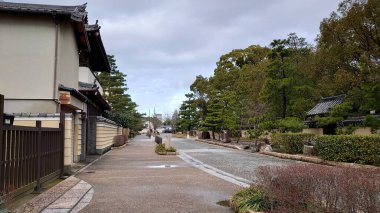 Fukuoka, Japonya - 01.28.2020: Hakata Tapınağı bölgesinde çalılar ve ağaçlarla birlikte bulutlu bir gökyüzünün altında geleneksel Japon evleri bulunan boş bir sokak