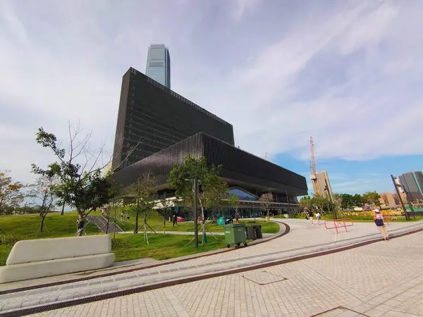 stock image Hong Kong - 08.29.2021: Wide-angle side view of the Mplus Museum with lawn surrounding and visitors walking on the walkway under a blue sky during the pandemic