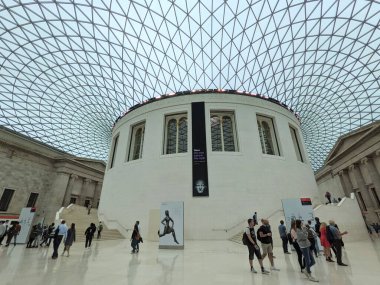 London, UK - 09.25.2021: Visitors walking in the Great Court of the British Museum under the curved tessellated glass roof during the pandemic under a grey sky clipart