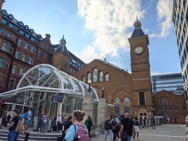 London, UK - 09.26.2021: Facade of the entrance of the Liverpool Street Station with passengers walking past and entering the station via an ironwork and glass structure under a blue sky clipart