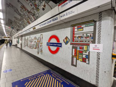 Londra, İngiltere - 11.04.2021: Tottenham Court Road İstasyonu 'ndaki Kuzey Hattı platformunda yürüyen yolcular Merkez Hattı ve renkli mozaik fayanslarla dekore edilmiş bir duvarın yanındaki çıkış yolu