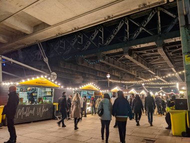 Londra, İngiltere - 12.21.2021: İnsanlar geceleyin Hungerford Köprüsü ve Southbank 'teki Golden Jubilee Köprüsü altındaki yoğun Noel Pazarı' na bakıyorlar