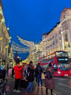 Londra, İngiltere - 12.21.2021: Regent Caddesi 'nde arabalarla ve yoldan geçen çift katlı otobüsle asılı duran melek Noel ışıklandırma dekorasyonunun fotoğraflarını çeken yayalar