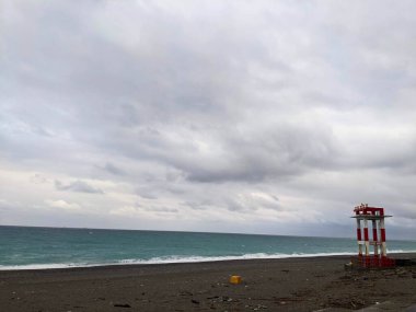 Hualien, Taiwan - 11.26.2022: A red and white metal structure with warning horns standing on the empty Qixingtan Beach facing the wavy Pacific Ocean on a stormy day under clouds during the pandemic clipart