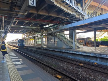 Hualien, Tayvan - 11.28.2022: Güneşli bir günde mavi bir tren karşı platforma yaklaşırken Hualien Tren İstasyonu 'nda yürüyen bir yolcu