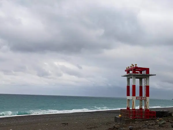 stock image Hualien, Taiwan - 11.26.2022: A red and white metal structure with warning horns standing on the empty Qixingtan Beach facing the wavy Pacific Ocean on a stormy day under clouds during the pandemic