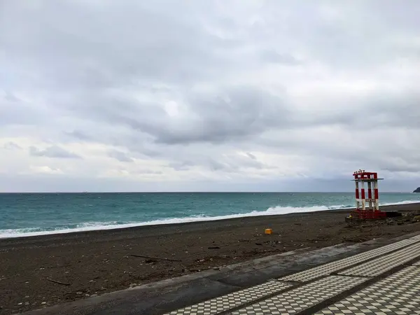 stock image Hualien, Taiwan - 11.26.2022: A red and white metal structure with warning horns standing on the empty Qixingtan Beach next to tiled steps facing the Pacific Ocean on a stormy day during the pandemic