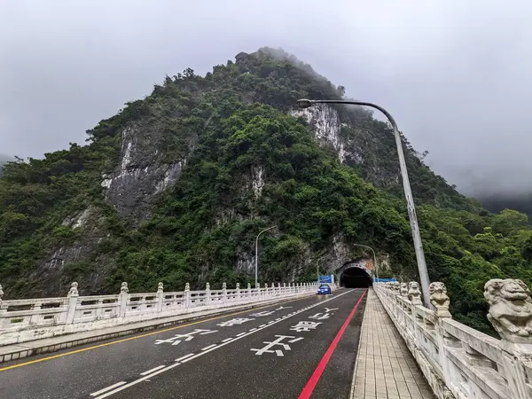 stock image Taroko, Taiwan - 11.26.2022: A car driving on the Shakadang Bridge next to the entrance to the Shakadang Trail after leaving the Shakadang Tunnel with a foggy mountain at the back during the pandemic