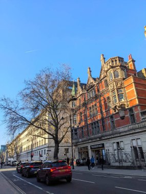 Londra, İngiltere - 03.18.2022: Salgın sırasında parlak mavi gökyüzü altında, Viktorya döneminden kalma kırmızı tuğlalı bir binada ve UCL kampüsünde kırmızı ışıkta bekleyen arabalar