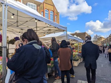 Londra, İngiltere - 04.03.2022: İnsanlar kalabalık Columbia Road Çiçek Pazarı 'ndaki salgın sırasında açık ve mavi bir gökyüzü altında çiçeklerle sokak satıcılarından saksı ve buketler satın alıyorlar