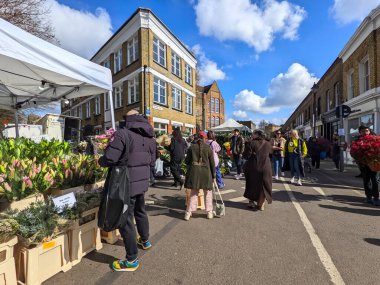 Londra, İngiltere - 04.03.2022: İnsanlar kalabalık Columbia Road Çiçek Pazarı 'ndaki salgın sırasında açık ve mavi bir gökyüzü altında çiçeklerle sokak satıcılarından saksı ve buketler satın alıyorlar