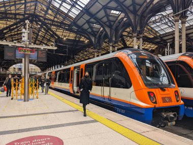 Londra, İngiltere - 04.03.2022: Trenden ayrılan ve platformda yürüyen yolcular, güneşli bir günde çelik ve cam çatı altında salgın sırasında Liverpool Caddesi İstasyonu 'na bir tren geldi.
