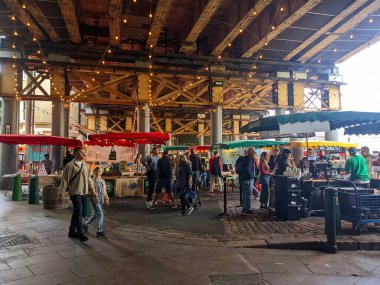 Londra, İngiltere - 05.07.2022: Güneşli bir günde Borough Market 'te tren yolu köprüsü altında kahve, taco ve meyve suyu satan ziyaretçiler