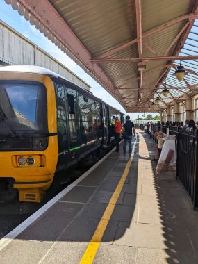 Windsor, İngiltere - 2022.07.16: Windsor ve Eton Merkez İstasyonu 'ndaki Great Western Demiryolu trenine binen yolcular, güneşli bir günde eski bir gölgelik ve lambalar altında lokomotif görüyorlar.