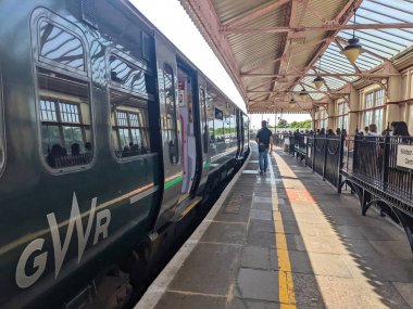 Windsor, İngiltere - 2022.07.16: Windsor ve Eton Merkez İstasyonu 'nda güneşli bir günde klasik bir gölgelik ve lambalar altında yolcuların trene binmesini bekleyen bir Great Western Demiryolu treni