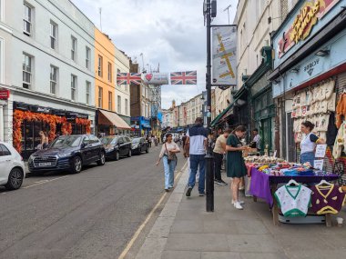 Londra, İngiltere - 2022.09.04: Portobello Market 'teki kaldırım taşıma taşıma çantalarına ve sokak satıcılarına göz gezdiren ziyaretçiler, Union Jack dekorasyonlarıyla bulutlu bir günde
