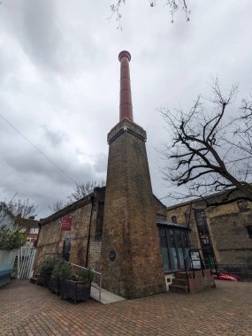Londra, İngiltere - 2023.03.07: Brunel Müzesi 'nin alçak açılı görüntüsü Thames Tüneli Lokomotifi, solunda duvar resmi olan tünel şaftı, giriş ve bulutlu bir gökyüzü altında merkezdeki bacayı restore etti