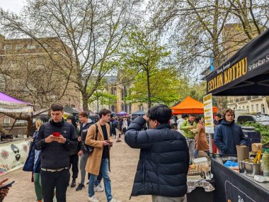 London, UK - 2023.04.27: People browsing and buying lunch from stalls in a food market in Torrington Square near UCL during the day under a cloudy sky clipart