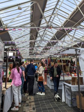 Londra, İngiltere - 2023.04.30: Ziyaretçiler, bulutlu bir günde Union Jack dekorasyon ve çatı pencereleri altında işlek Greenwich Pazarı 'nda el sanatları ve aksesuarları satan pazar tezgahlarına göz atıyorlar