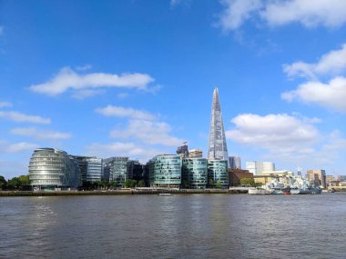 London, UK - 2023.05.26: Modern London skyline featuring The Shard and River Thames along The Queens Walk from Potters Fields Park with HMS Belfast on the side under a blue sky on a sunny day clipart