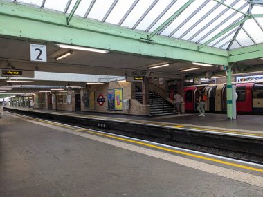 Londra, İngiltere - 2023.07.08: Beyaz Şehir İstasyonu 'ndaki Central Line treninden inen yolcular, açık yeşil metal bir tepe örtüsünün altında, boş platformlarla 