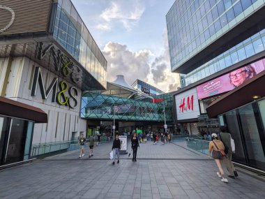 Londra, İngiltere - 2023.07.09: Westfield Stratford City 'ye köprü üzerinden giren ve çıkan müşteriler, Stratford İstasyonu, mağaza, moda mağazası ve günbatımına yakın reklam