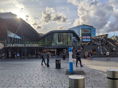 London, UK - 2023.07.09: Ground-level entrance to Stratford Station with stairs and escalators leading to Westfield Stratford City at the back near sunset with sunbeam and silhouette of clouds clipart