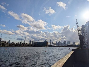 London, UK - 2023.07.12: Converted historic warehouses, Stothert and Pitt cranes, and Newham City Hall over Royal Victoria Dock under a blue sky with silhouette of clouds under sunlight  clipart