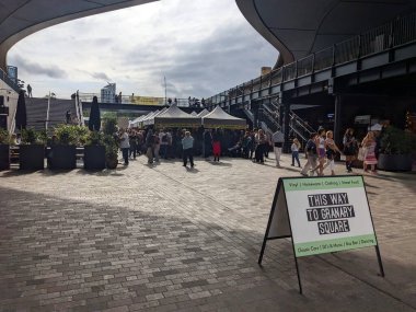 Londra, İngiltere - 2023.10.01: Coal Drops Yard 'daki Granary Square pazarına giriş, müşteriler bulutlu bir gökyüzü altında klasik ve ikinci el ürünler satarak iki dizi pazar tezgahına göz atıyorlar