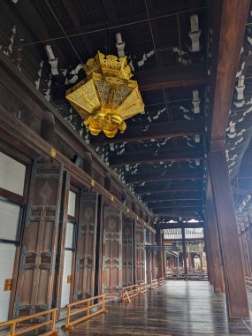 Kyoto, Japan - 2023.12.14: An empty wooden corridor alongside doors and pillars under a golden ornated lantern hanging from the ceiling in the Hongan-ji Goeido of Nishi Hongan-ji clipart