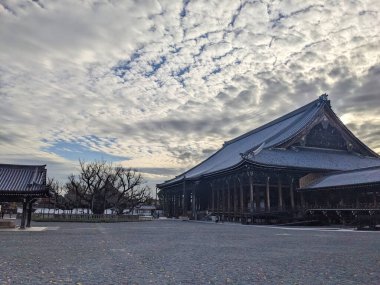 Kyoto, Japonya - 2023.12.14: Nishi Hongan-ji Goeido 'daki ahşap bir gökyüzü altında bulutlar ve arkalarındaki güneş ışığından gelen siluetleri ile sessiz bir sahne