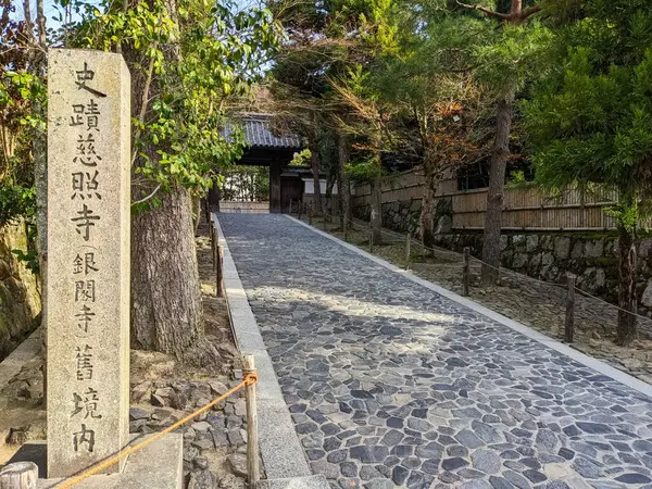 Kyoto, Japonya - 2023.12.18: Ginkaku-ji 'nin girişine giden ağaçlı bir patika, güneş ışığı altında oyulmuş bir stele' nin yanında.