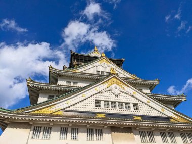 Osaka, Japonya - 12.21.2023: Osaka Kalesi 'nin ön cephesi, altın süslemeler, beyaz duvar ve güneşli mavi gökyüzünün altında geleneksel çatı