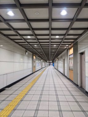 Osaka, Japonya - 30.12.2023: Kintetsu Nippombashi İstasyonu 'ndaki sessiz bir yeraltı geçidinde, tünelin diğer ucunda fayanslı zemin ve tavan lambalarının altında sadece bir yolcu yürüyor.