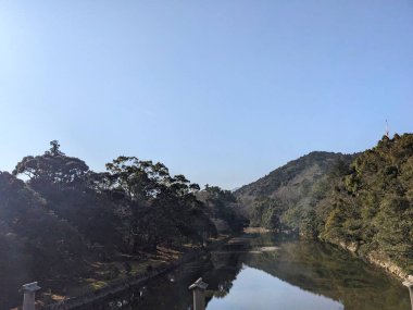 Ise, Japan - 30.12.2023: Riverbank of Isuzu River alongside trees under a clear blue sky in Naiku, the inner shrine of the Ise Grand Shrine, view from the Uji Bridge clipart