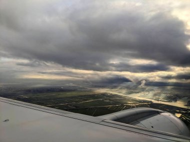 Amsterdam, Hollanda - 12.13.2023: Çarpıcı bulutlar ve güneş ışınlarıyla kesişen su yolları ve tarlalar üzerindeki bir uçaktan hava görüntüsü