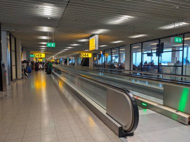 Amsterdam, Netherlands - 12.13.2023: Interior of Amsterdam Airport Schiphol terminal boarding gate next to the waiting area and two movable walkways full of tourists and travellers clipart