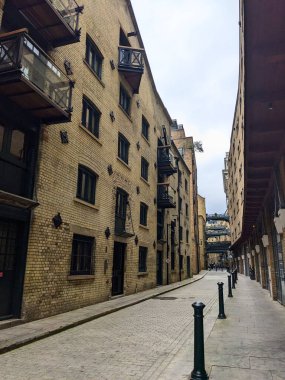 Londra, İngiltere - 05.13.2024: Shad Thames 'in sakin bir zamanı dönüştürülmüş depolarla ve fayanslı zemin üzerinde yükseltilmiş geçitlerle ve turistler olmadan bulutlu bir gökyüzünün altında zemin kattaki dükkanlarla