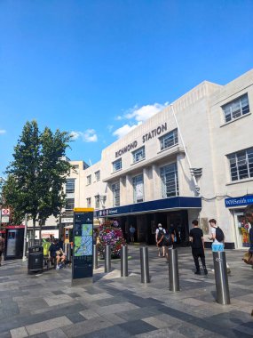 Londra, İngiltere - 07.19.2024: Art Deco Richmond İstasyonu girişinin ön cephesinde bir yaz öğleden sonra açık mavi gökyüzü altında bir otobüs durağının yanındaki kaldırımdan giren yolcular