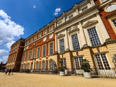 Londra, İngiltere - 07.19.2024: Kırmızı tuğla önünde yürüyen ve Hampton Court Palace 'da açık mavi gökyüzü altında güneşli bir yaz öğleden sonrasında Güney Cephesi' ni süsleyen ziyaretçiler
