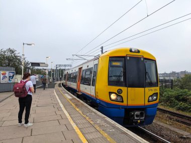 Londra, İngiltere - 08.02.2024: Willesden Junction İstasyonu 'ndaki platforma yaklaşan bir Londra metro treni, yolcular bulutlu bir gökyüzünün altında en yoğun saatlerinde binmek için beklerken,