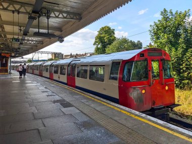 London, UK - 08.02.2024: A Bakerloo Line train approaching the platform at Willesden Junction Station when passengers waiting to get on during morning peak hours under a blue sky with clouds clipart