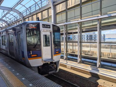 Rinku Town, Japan - 08.13.2024: A Nankai Airport Line train heading to Kansai Airport approaching the platform at Rinku-town Station under a clear blue sky with sunlight in the summer clipart